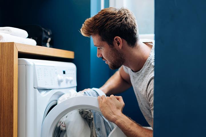 man putting laundry into dryer
