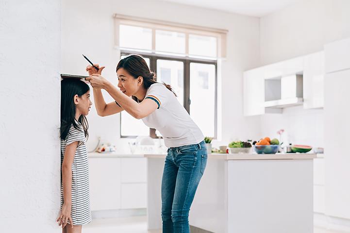 mother measuring the height of her daughter on the kitchen wall