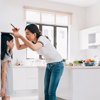 mother measuring the height of her daughter on the kitchen wall