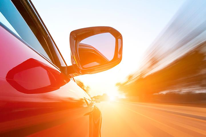 passenger side view of speeding red car driving into the sun