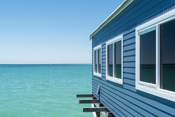 side of a blue building with white windows jutting out into the water