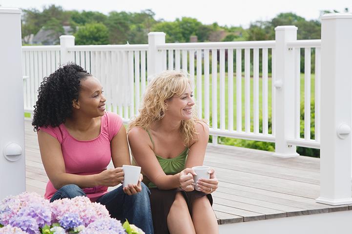 two women sitting on a porch holding coffee cups hydrangeas in the foreground