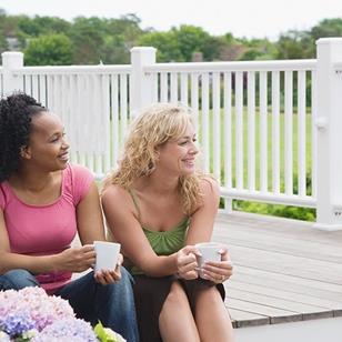 two women sitting on a porch holding coffee cups hydrangeas in the foreground