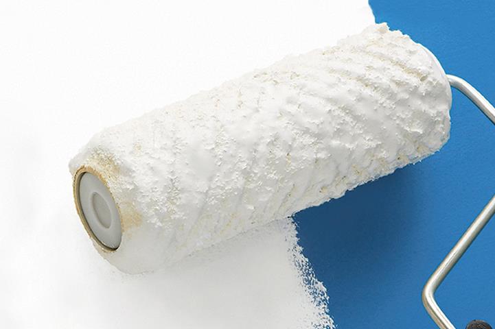 white paint covered paint roller spreading paint on blue wall
