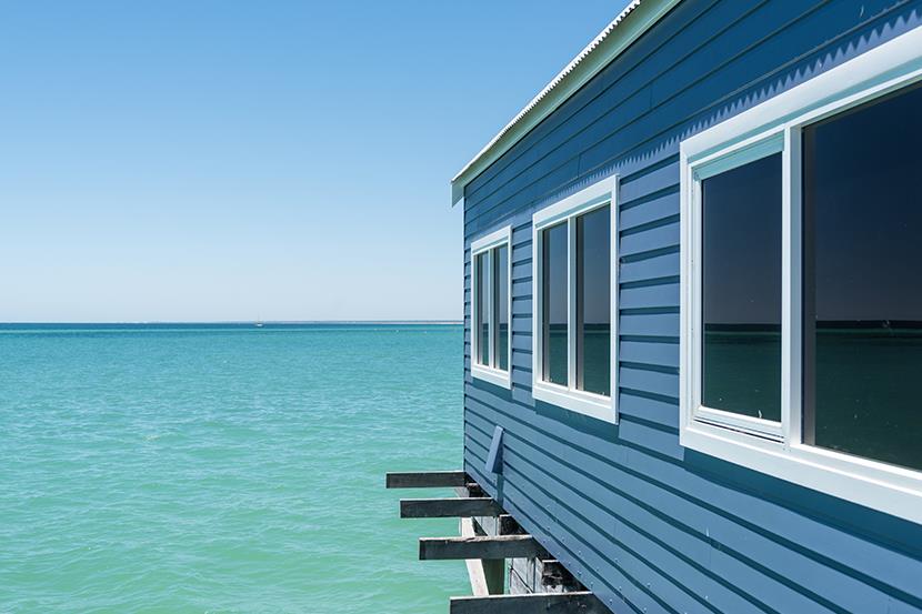 side of a blue building with white windows jutting out into the water