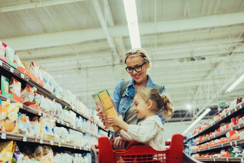 mother pushing shopping cart with daughter seated and holding a box