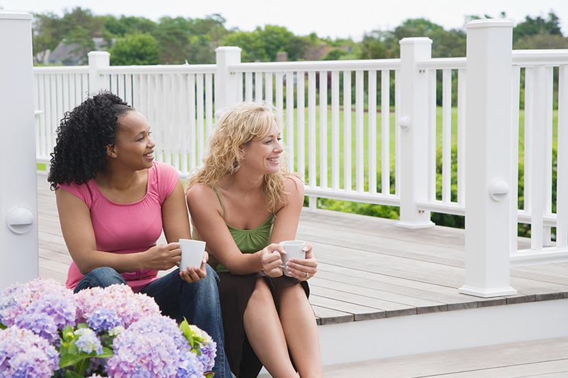 two women sitting on a porch holding coffee cups hydrangeas in the foreground