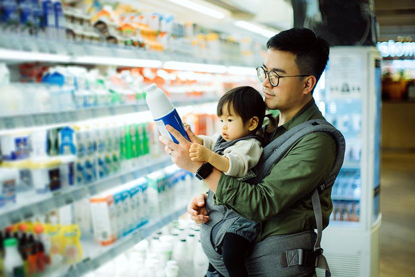 father holding little daughter in carrier shopping in supermarket dairy aisle