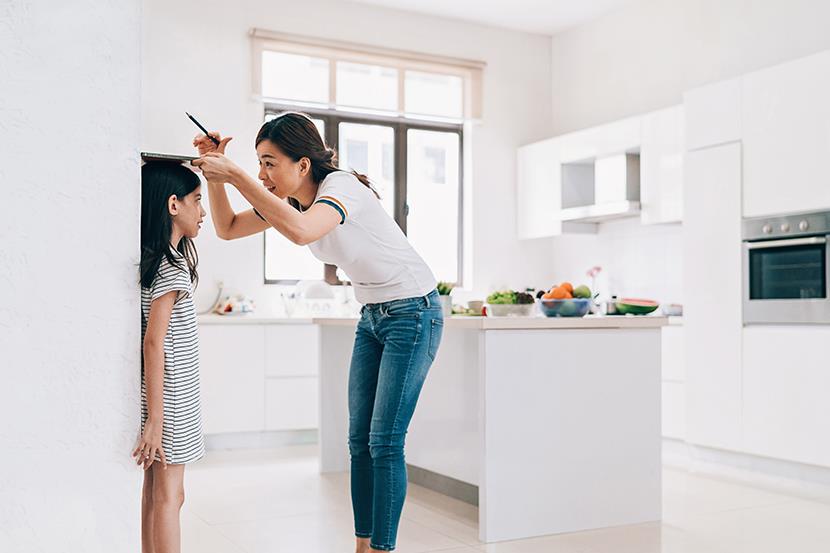 mother measuring the height of her daughter on the kitchen wall