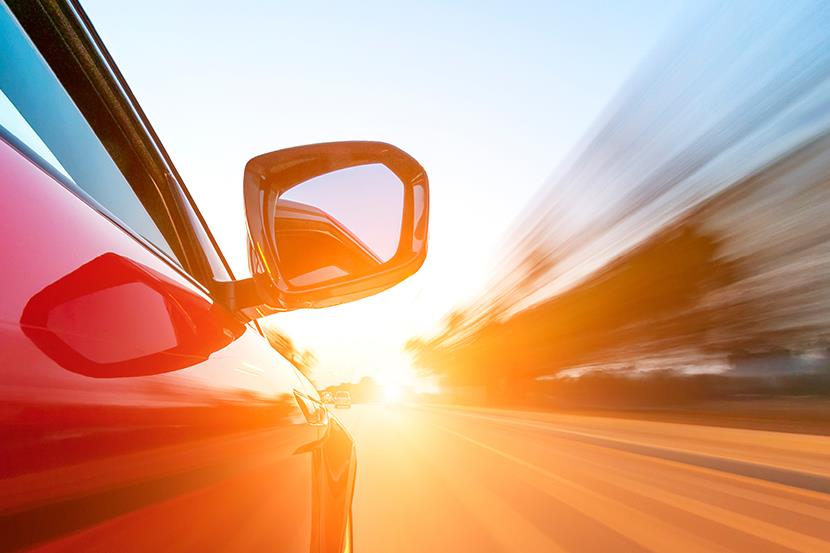 passenger side view of speeding red car driving into the sun