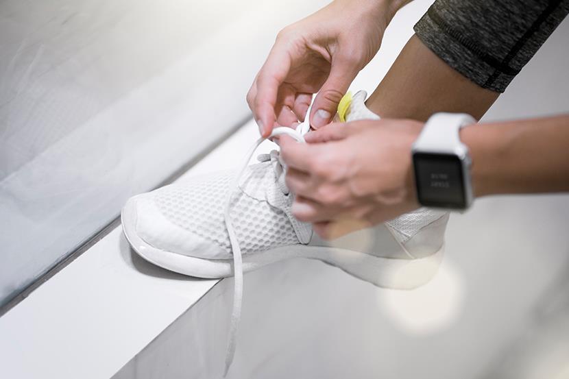 person wearing smartwatch tying laces of white sneaker