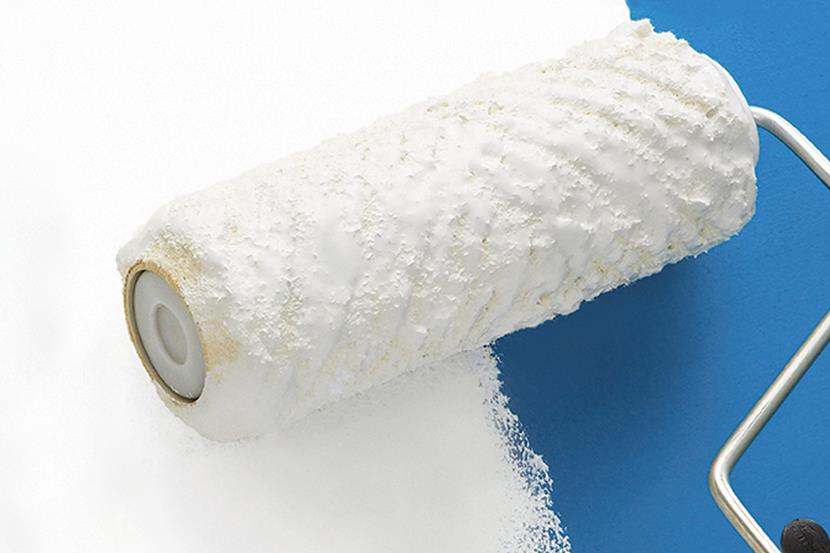 white paint covered paint roller spreading paint on blue wall